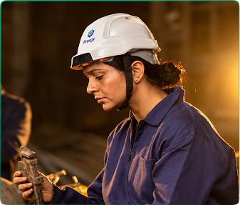 A woman in a Proxgy helmet working on a machine part in warm light
